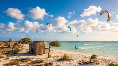 Kitesurfers and a beach cabana on a windy, sunny day in Aruba, illustrating the islands consistent trade-wind weather