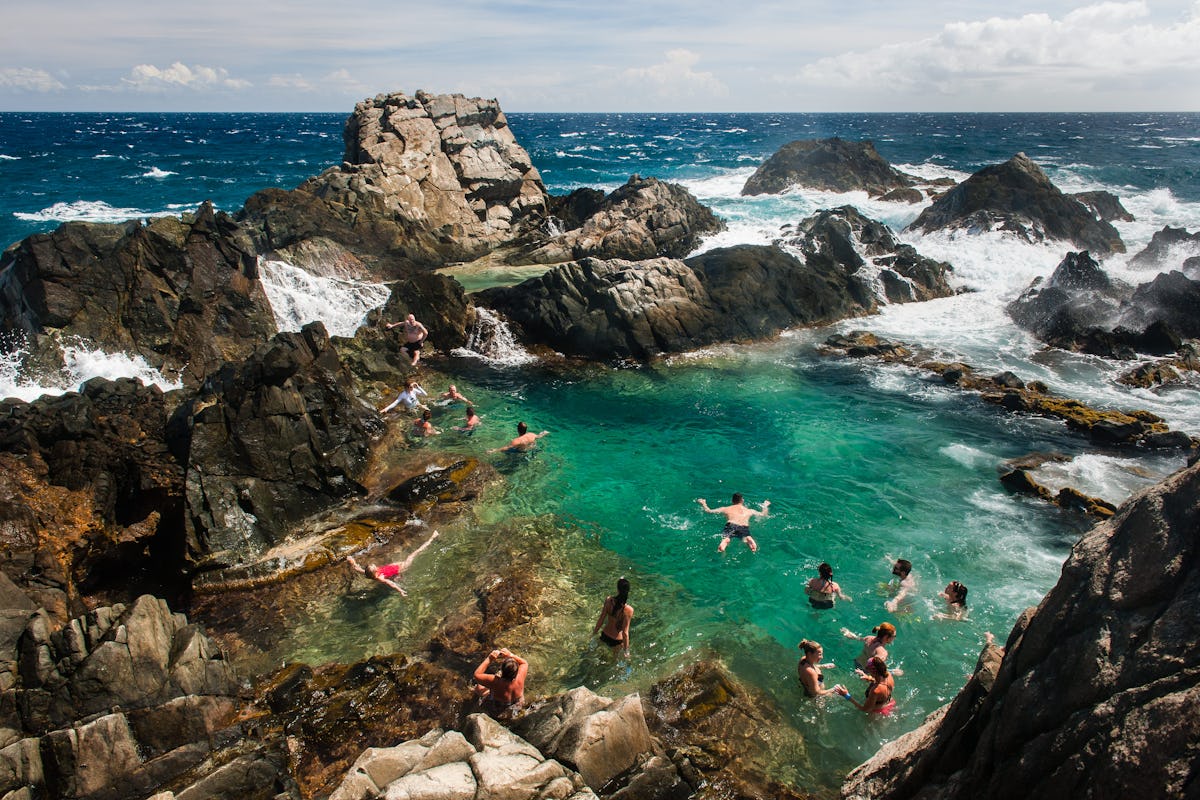 Visitors swimming in Aruba's Natural Pool (Conchi), a volcanic rock basin in Arikok National Park