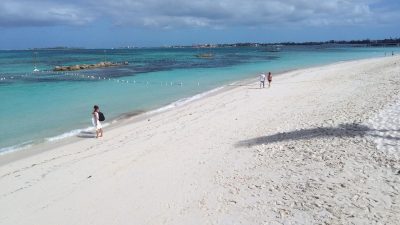 A calm turquoise-water beach near Nassau with a few people walking along the sand under a partly cloudy sky