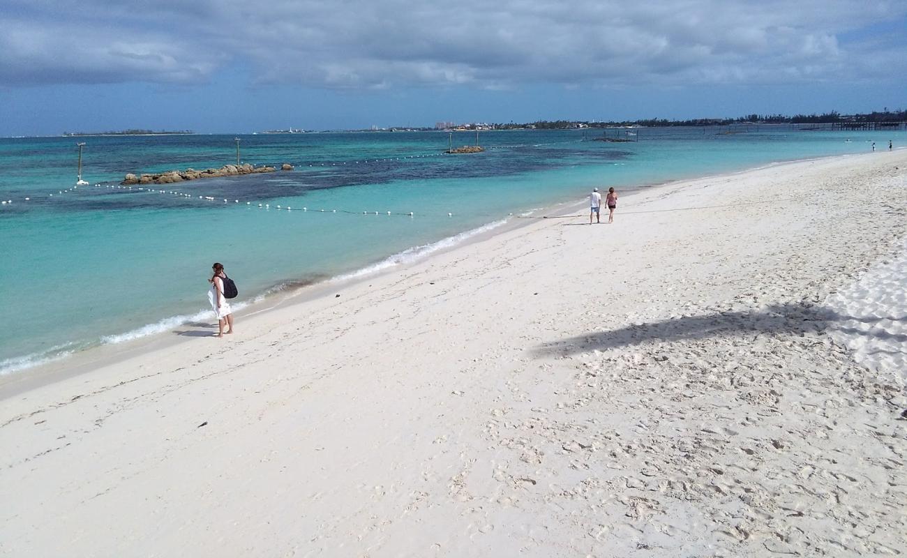 A calm turquoise-water beach near Nassau with a few people walking along the sand under a partly cloudy sky