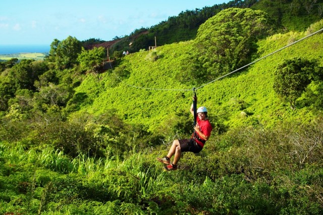 Teen ziplining through lush green hillside in West Maui