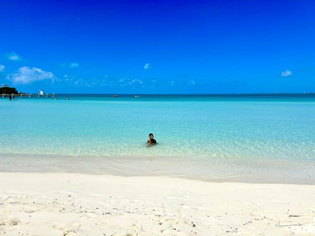 Calm, shallow turquoise water at Sapodilla Bay Beach, Providenciales, with someone wading